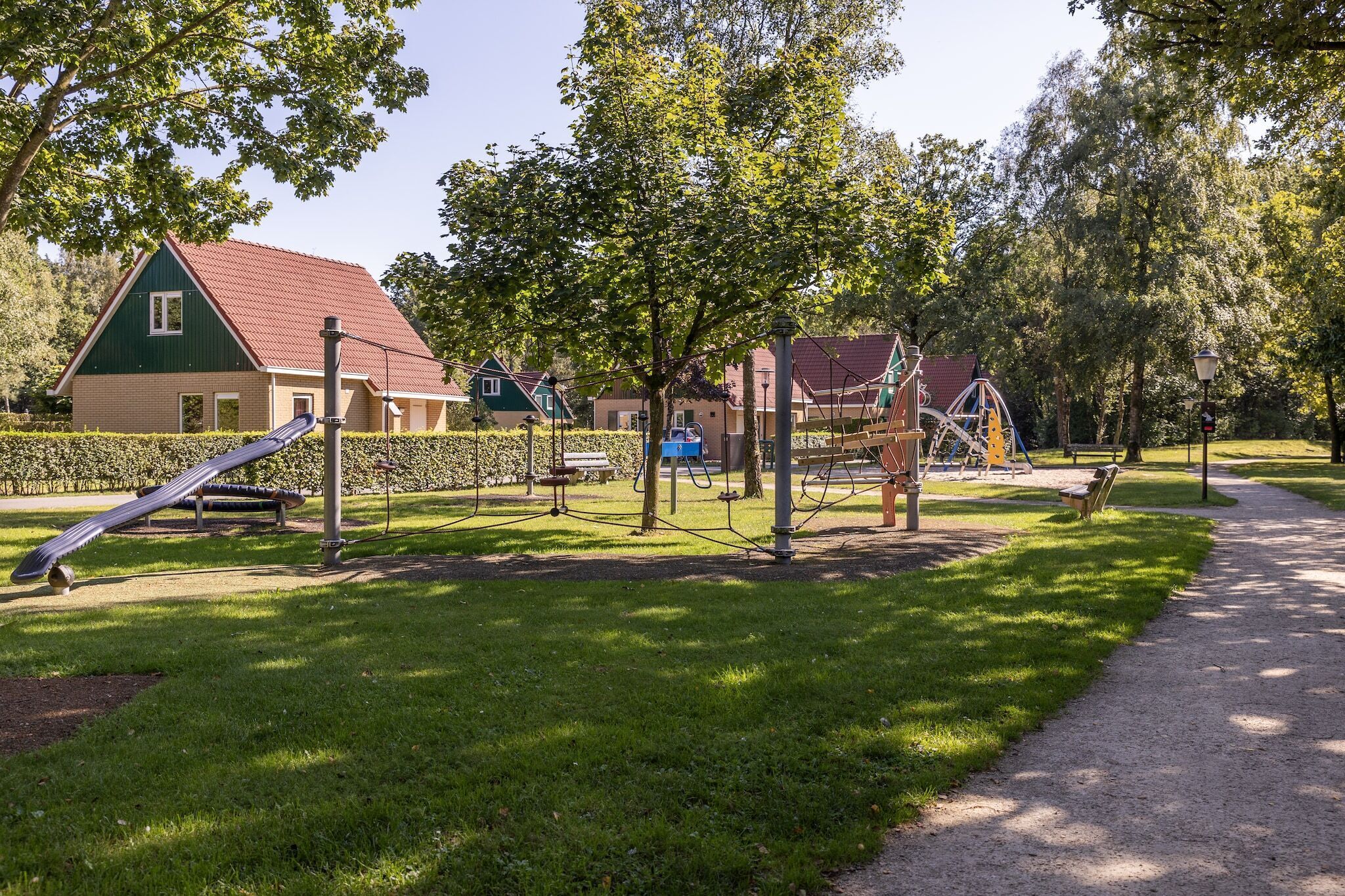 En park med legeudstyr, en sti og en bygning med rødt tag.