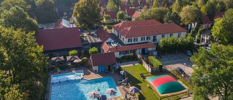 Vista aérea de una zona residencial con piscina, varias casas y un edificio grande con techo rojo.