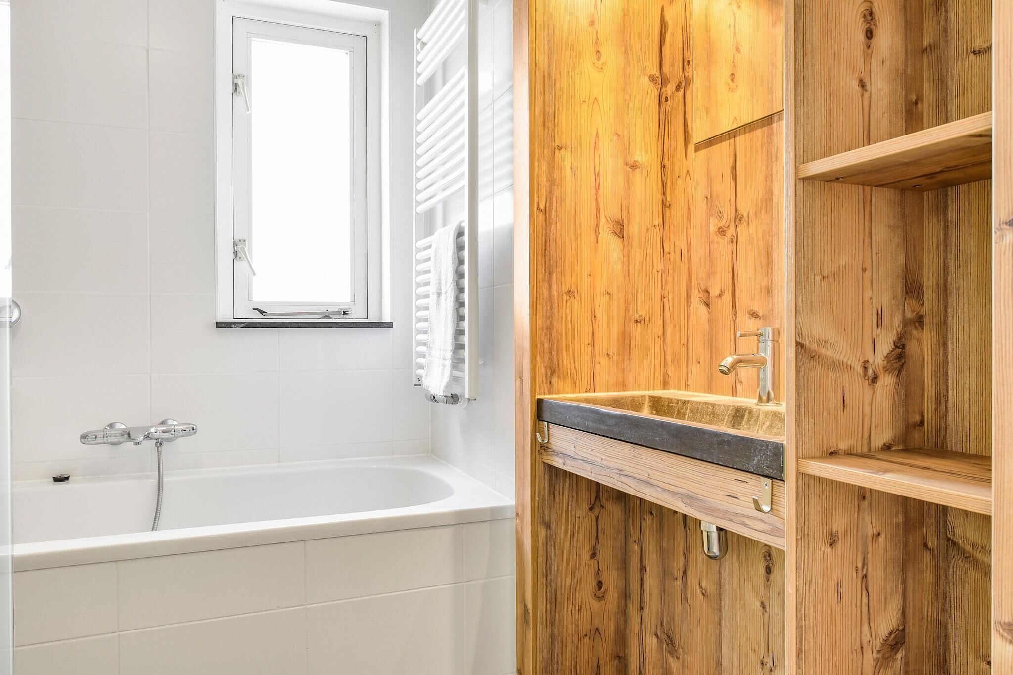A bathroom with a white bathtub, a window, and wooden paneling.