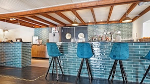 Eine Bar mit blauen Barhocker, einer Ziegelrückwand und Holzbalken an der Decke.