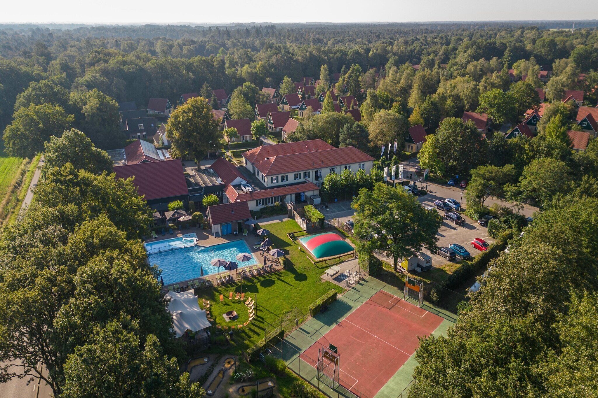 Vue aérienne d’un quartier résidentiel avec des maisons, une piscine et un court de tennis.