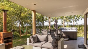 An outdoor patio with a sofa, chairs, a table, a hot tub, and a wood-burning stove.