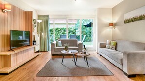A modern living room with a flat-screen TV, a sofa, a coffee table, and a dining table. - Holiday Home in Diessen near Tilburg (Diessen-Baarschot)