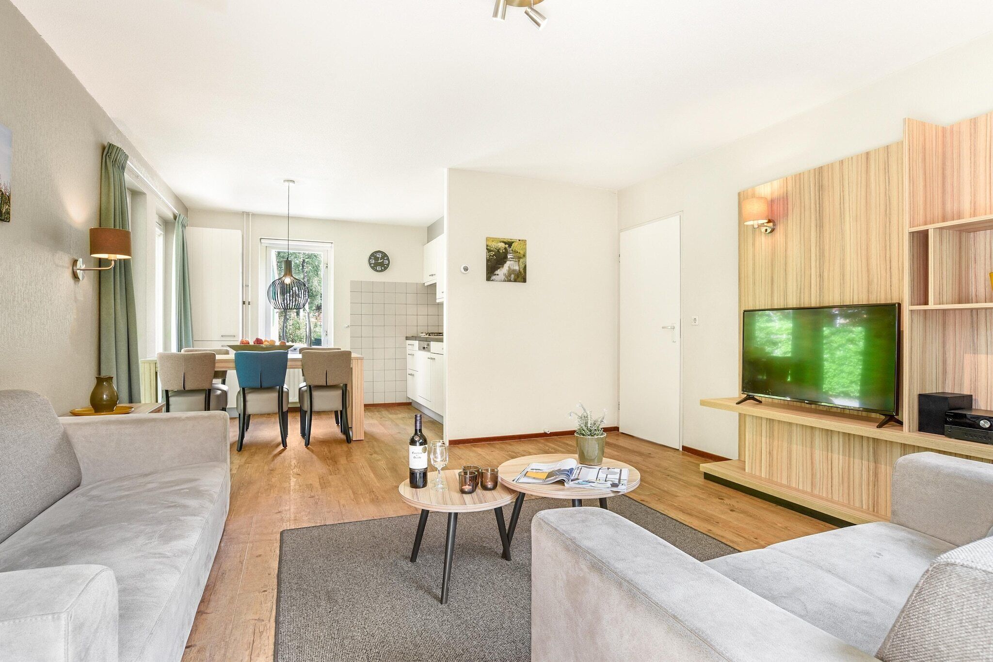 A modern living room with a sofa, coffee table, and TV. There is a dining area with chairs and a table.