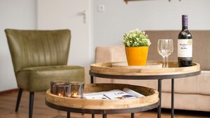 A wooden tray with a bottle of Casillero del Diablo wine, a glass, and a small potted plant on a round table. - Holiday Home in Brabant with Garden & BBQ (Diessen-Baarschot)