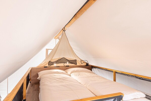 Una cama individual con estructura de madera y dosel, ubicada en una estructura parecida a una tienda de campaña con interior blanco.