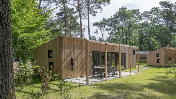 A modern wooden cabin with a patio area, surrounded by trees. - Air-Conditioned Chalet near Eindhoven (Mierlo)