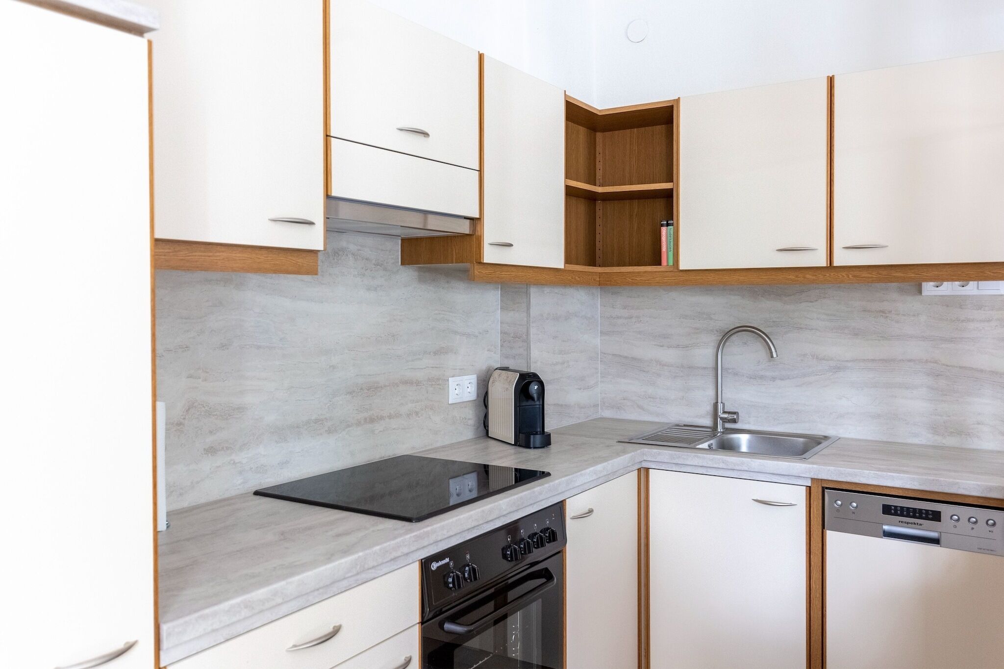 Een moderne keuken met witte kasten, een zwarte inductiekookplaat, een inbouwoven, een koffiezetapparaat en een vaatwasser.