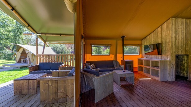 A covered outdoor seating area with wooden furniture, a fire pit, and a view of the surrounding garden.