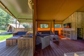 A covered outdoor seating area with wooden furniture, a fire pit, and a view of the surrounding garden.