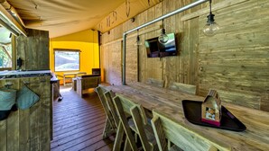 Ein rustikales Holzinterieur mit einem langen Esstisch, Bänken, einer kleinen Küchenzeile und einem an der Wand befestigten Fernseher.