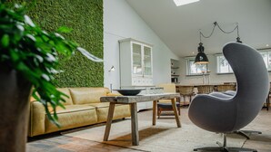 Un salon moderne avec un mur vert, un canapé jaune, un fauteuil rond gris et une table en bois.