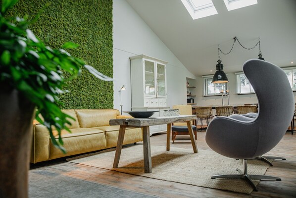 Un salon moderne avec un mur vert, un canapé jaune, un fauteuil rond gris et une table en bois.