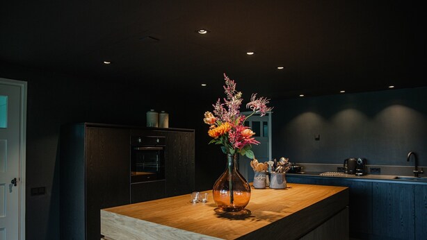 Une cuisine moderne avec un îlot central en bois, des meubles de rangement aux couleurs sombres et un vase rempli de fleurs.