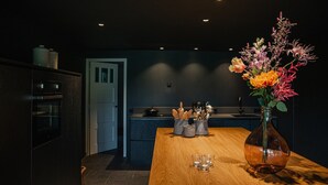 Une cuisine moderne avec des meubles de couleur sombre, une table à manger en bois et un vase rempli de fleurs.