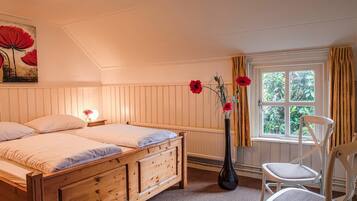 Une chambre à coucher avec un lit en bois, une table de chevet, un vase de fleurs et une fenêtre avec des rideaux.