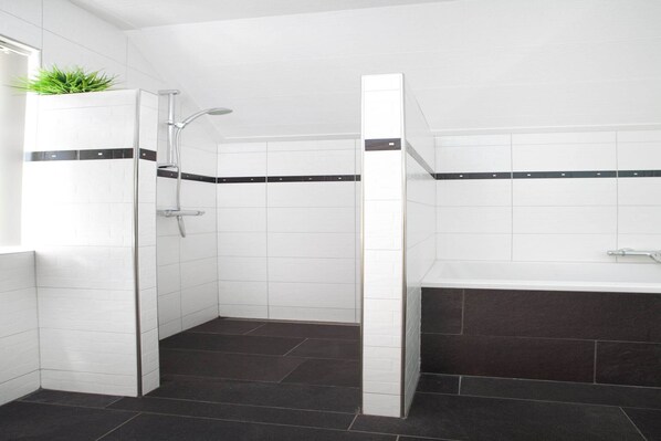 A modern bathroom with a shower, a bathtub, and a potted plant.