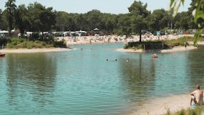 A lakeside beach with people swimming and sunbathing, surrounded by trees and beach umbrellas. - Spacious Villa in Forest Park (Schaijk)