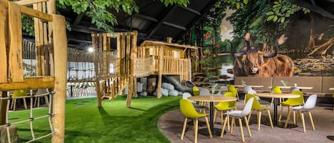 An indoor restaurant with a rustic wooden structure, green artificial grass, and yellow and white chairs.