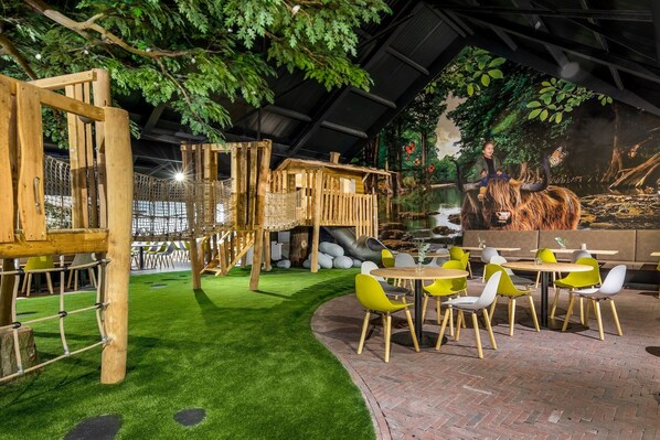An indoor restaurant with a rustic wooden structure, green artificial grass, and yellow and white chairs.