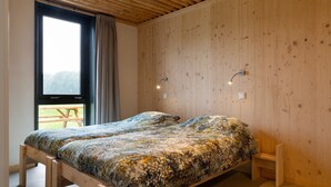 Ein Einzelbett mit Blumendecke in einem Zimmer mit Holzwänden und einem großen Fenster.