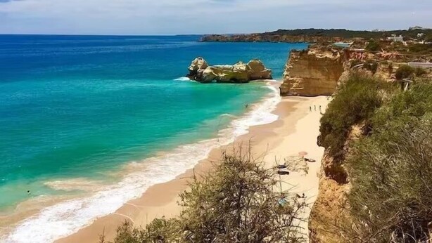 A coastal beach with clear turquoise waters, sandy shores, and rocky cliffs.