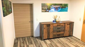 Un couloir avec une porte en bois, un meuble en bois doté de tiroirs et deux tableaux encadrés accrochés au mur.