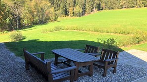 Une table et des bancs en bois sont disposés sur un chemin de gravier, avec un champ herbeux et des arbres en arrière-plan.
