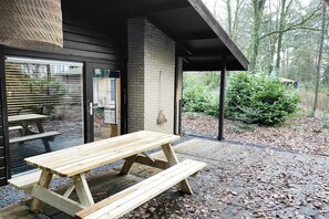 A wooden picnic table with benches, a brick wall, and a hanging light fixture. - Holiday Home in Rheezerveen with Sauna & Hot Tub (Rheezerveen)