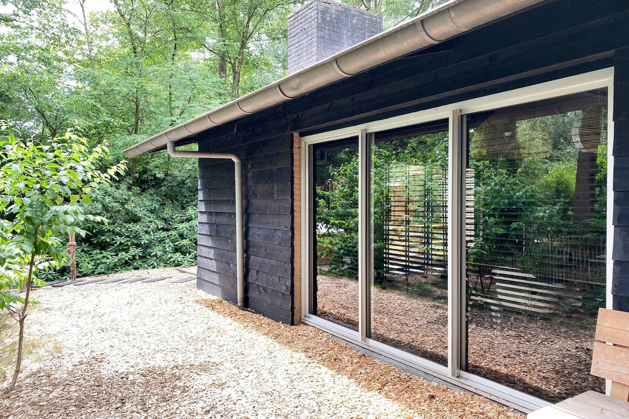 Un bâtiment moderne doté de grandes fenêtres en verre, d’une allée en gravier et d’une terrasse en bois.