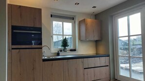 Eine moderne Küche mit Holdelementen, einem eingebauten Backofen und einem großen Fenster mit Blick ins Freie.
