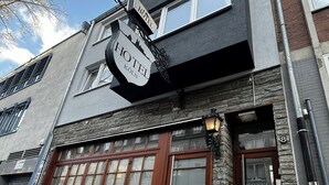 Une enseigne d’hôtel portant l’inscription « HOTEL KÖLN », fixée à un bâtiment doté d’une façade en pierre et de grandes fenêtres.