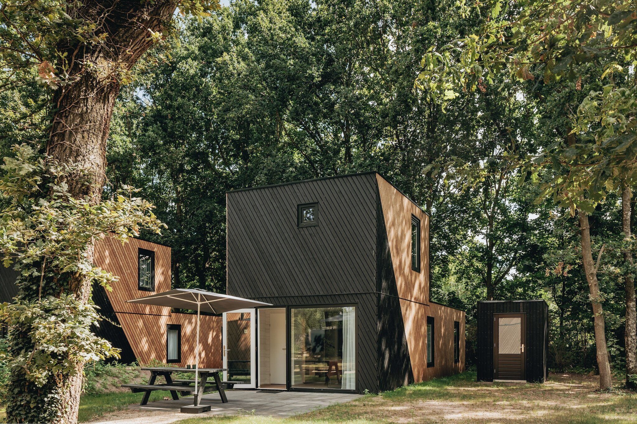 Een moderne, tweelaagse hut met een ruime glazen deur, omringd door dicht bos.