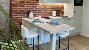 A kitchen with a brick wall, white cabinets, and a wooden floor.