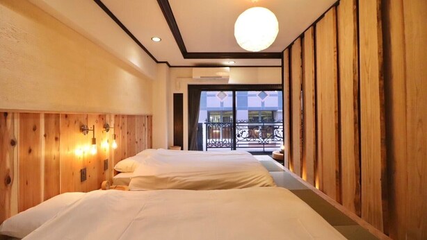Habitación de hotel con dos camas, paneles de madera en las paredes, un balcón con vistas y una lámpara de techo redonda.