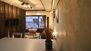 Un comedor con una mesa blanca, sillas, una planta en maceta y un balcón con barandilla.