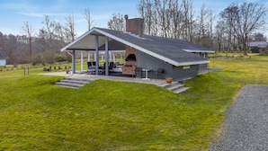 A modern house with a covered patio, a brick fireplace, and a well-maintained lawn.