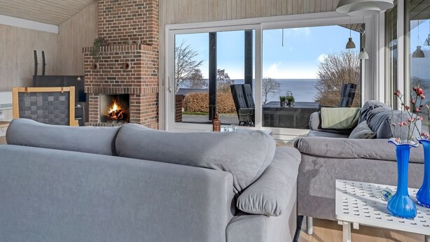 A modern living room with a fireplace, grey sofas, and a view of the sea.