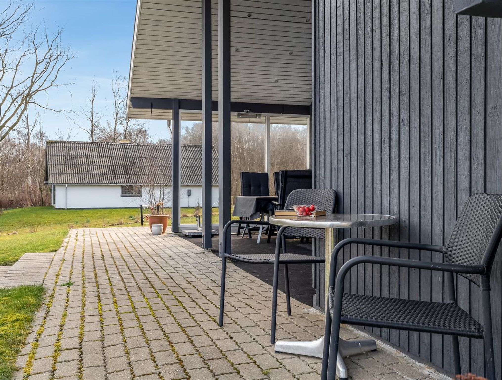 An outdoor patio area with a table and chairs, a potted plant, and a view of a house in the background.