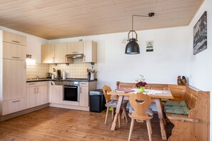 Une cuisine avec des meubles de rangement en bois, une table à manger avec des chaises, un banc et un luminaire suspendu.