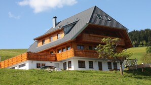 A two-story wooden house with a sloped roof, a balcony, and a chimney. - Apartment 'Sonnenblick, 54sqm' with Shared Terrace, Garden, and Wi-Fi (Schonach)