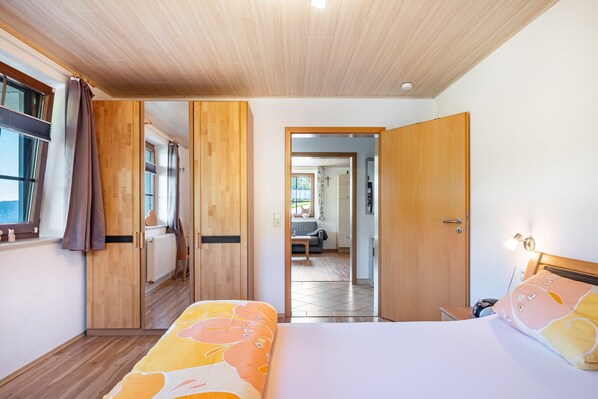 Une chambre d’hôtel avec un lit, une armoire en bois et une vue sur une autre chambre, accessible par une porte ouverte.