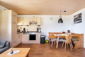 Une cuisine compacte avec des meubles en bois, un coin repas avec un banc et une horloge au mur.