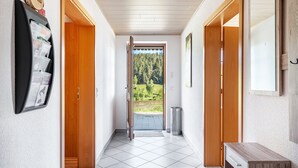 A hallway with wooden doors, a magazine rack, and a view of a forest through a glass door. - Apartment 'Sonnenblick, 54sqm' with Shared Terrace, Garden, and Wi-Fi (Schonach)