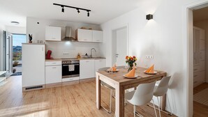 A modern kitchen with white cabinets, a wooden dining table, and a view of the outdoors. - Cozy Apartment in Oberkirch – Enjoy Nature & Central Location (Oberkirch)