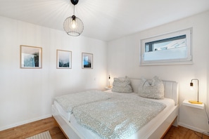 Une chambre à coucher avec un lit, des lampes de chevet, une fenêtre et trois tableaux encadrés accrochés au mur.