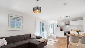 A modern living room with a dark sofa, a dining area with two chairs, and a kitchen with white cabinets. - Cozy Apartment in Oberkirch – Enjoy Nature & Central Location (Oberkirch)