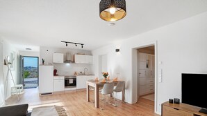 A modern kitchen with white cabinets, a dining area with a table and chairs, a sofa, and a TV on a wooden stand. - Cozy Apartment in Oberkirch – Enjoy Nature & Central Location (Oberkirch)