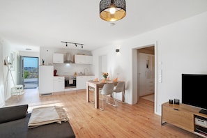 Eine moderne Küche mit weißen Schränken, einem Essbereich mit Tisch und Stühlen, einem Sofa und einem Fernseher auf einem Holzboden.