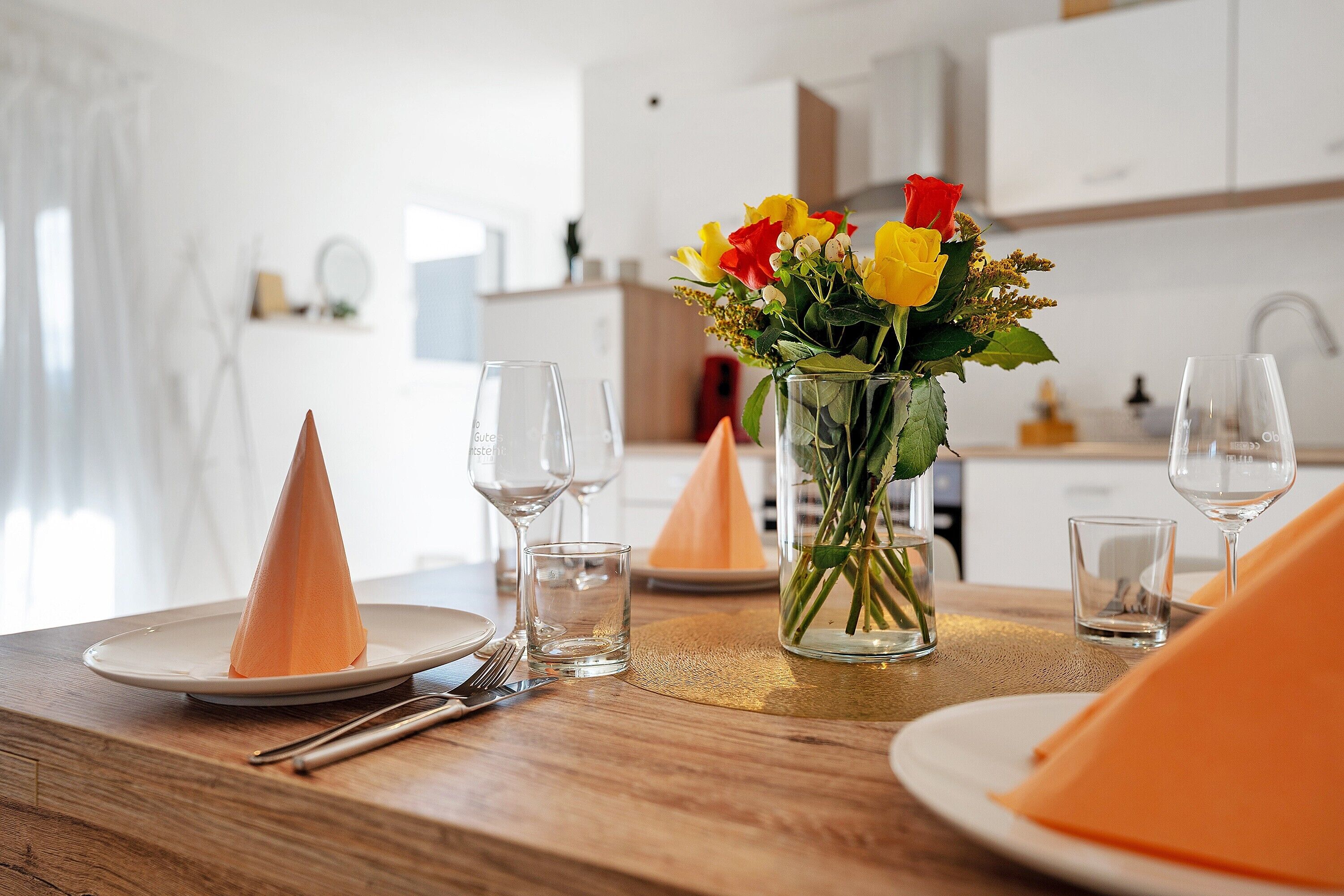 A dining table set with plates, glasses, and a vase with flowers.